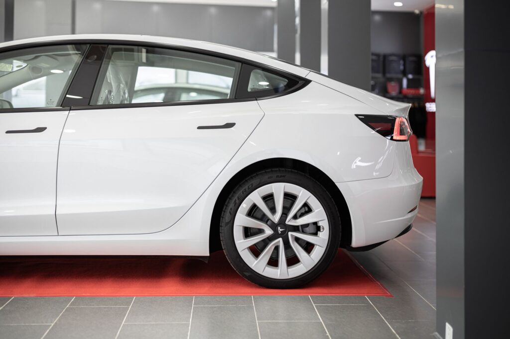 A modern white electric car showcased on a red carpet inside a showroom.