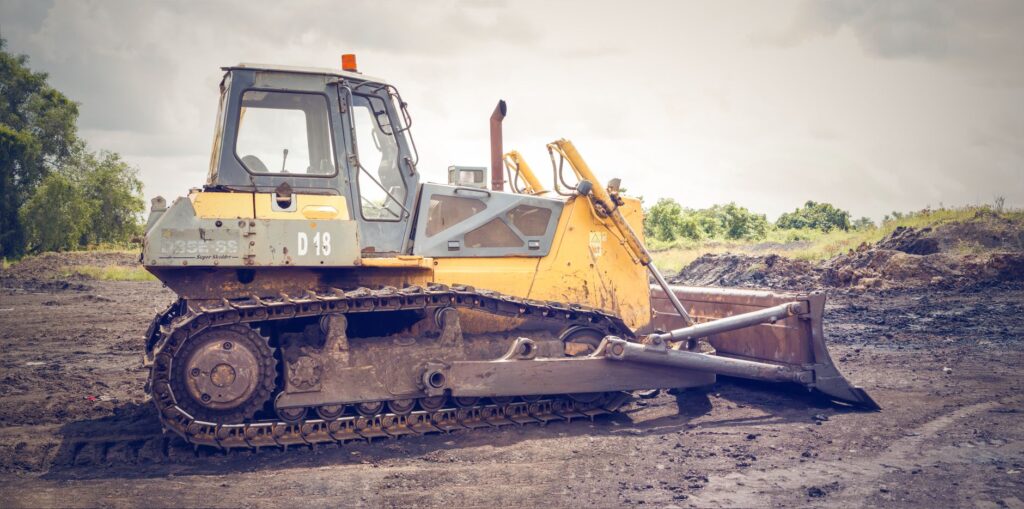 A powerful bulldozer on muddy construction ground under a cloudy sky.