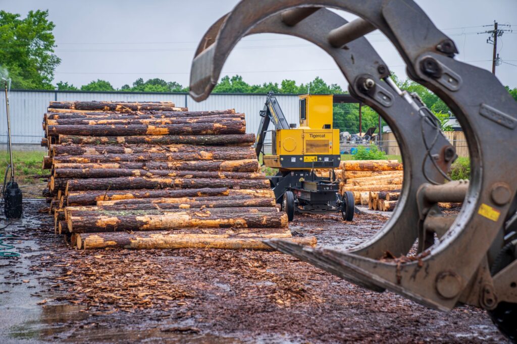 Heavy machinery stacking timber logs at an industrial site amid a natural backdrop.