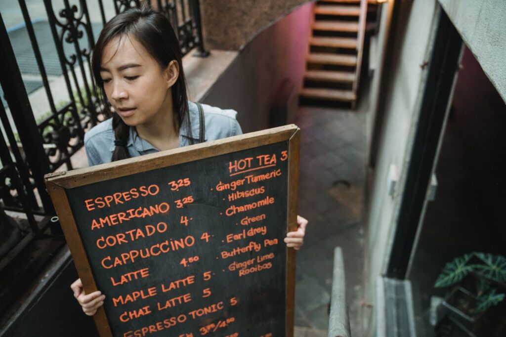 A barista holding a chalkboard menu at an outdoor café entrance.