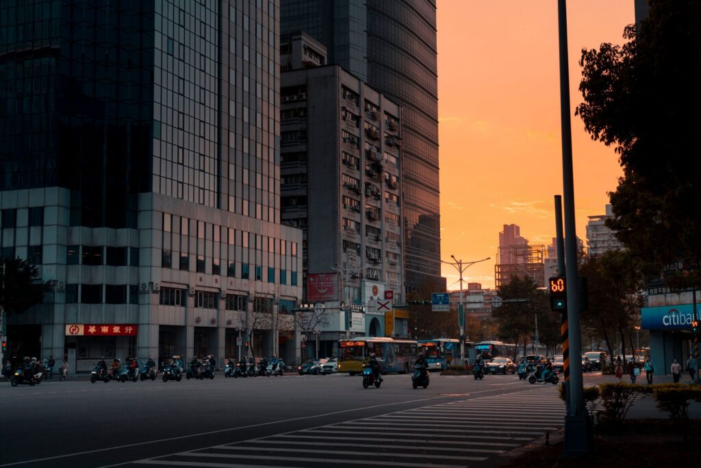 A bustling city street scene at sunset with traffic and modern skyscrapers.