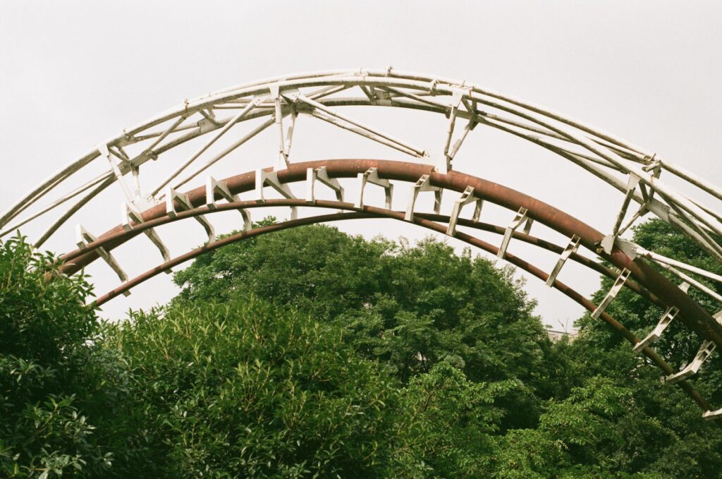 A close-up view of a steel roller coaster arch surrounded by lush summer foliage.