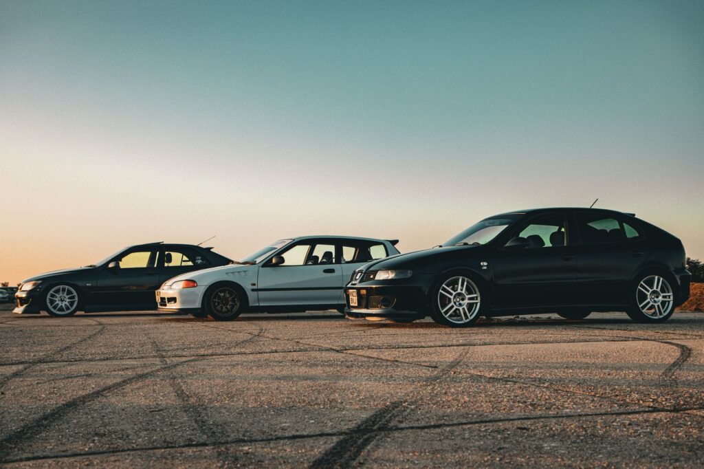 Three tuned sports cars parked on asphalt at sunset, showcasing vehicle customization and style.