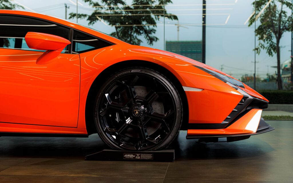 Close-up of an orange Lamborghini Huracan Tecnica's wheel and body detail at an indoor auto exhibition.