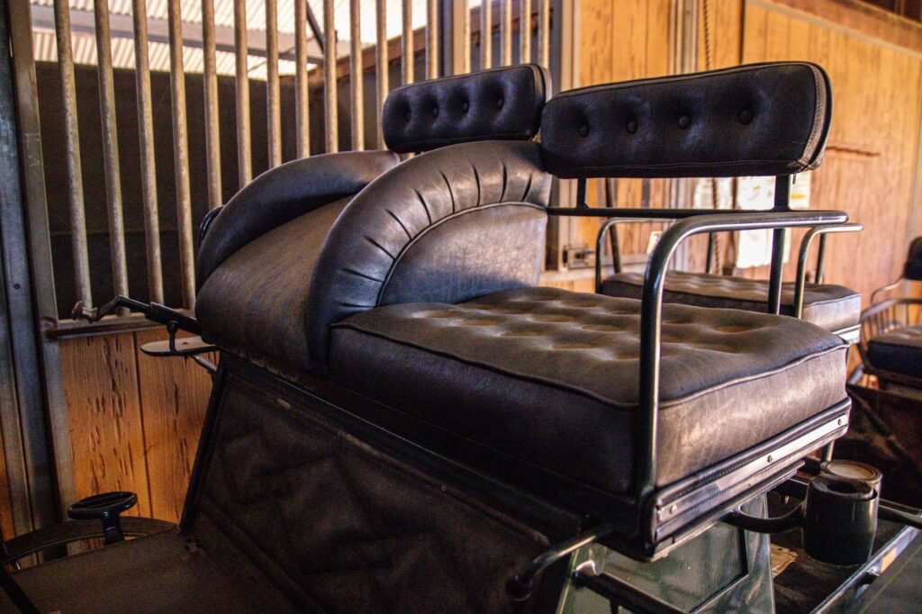 A classic leather carriage seat set against a rustic wooden barn interior, exuding vintage charm.