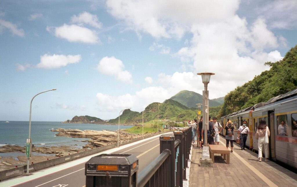 Peaceful view of a coastal railway station in Taipei, Taiwan, with mountains and ocean.