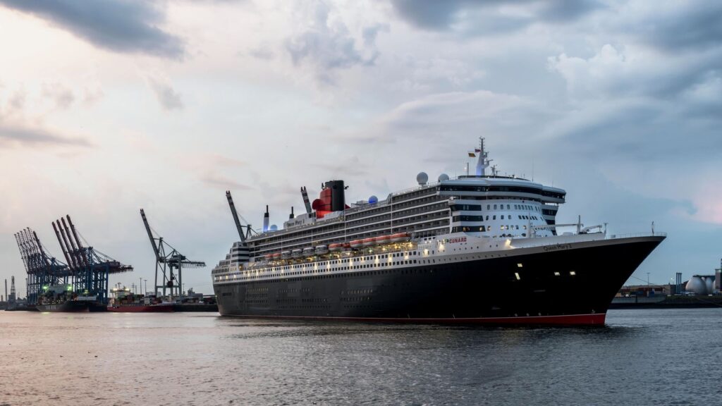 Queen Mary 2 at Hamburg Harbor surrounded by cranes and calm waters under a morning sky.