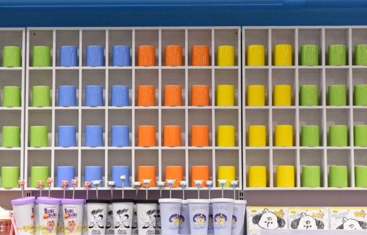 Vibrant shelf of colorful cups in a retail store, organized by color and showcasing a playful design.
