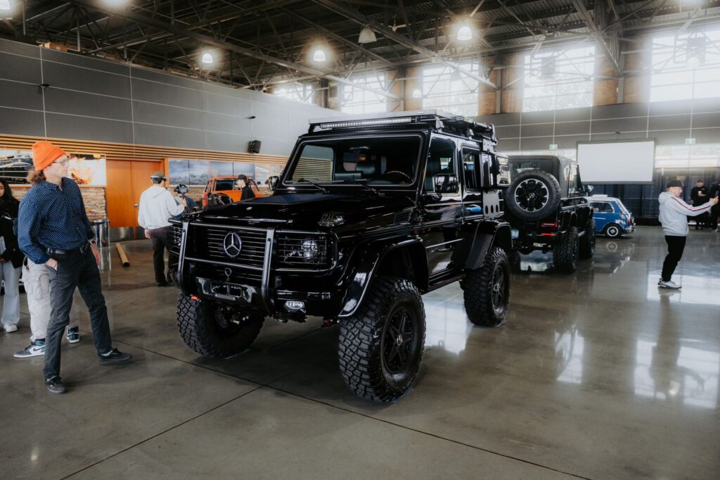 Luxury black SUV showcased at an indoor auto exhibition with people admiring the vehicles.