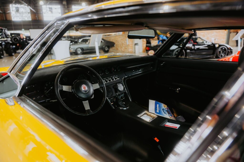 Interior view of a classic yellow sports car with visible steering wheel at an auto exhibition.