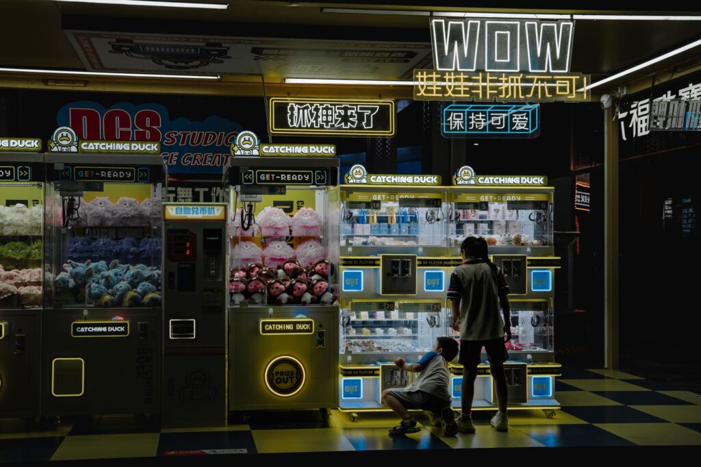 Kids enjoying claw machines at night in a vibrant arcade setting. Captures the lively and colorful ambiance.