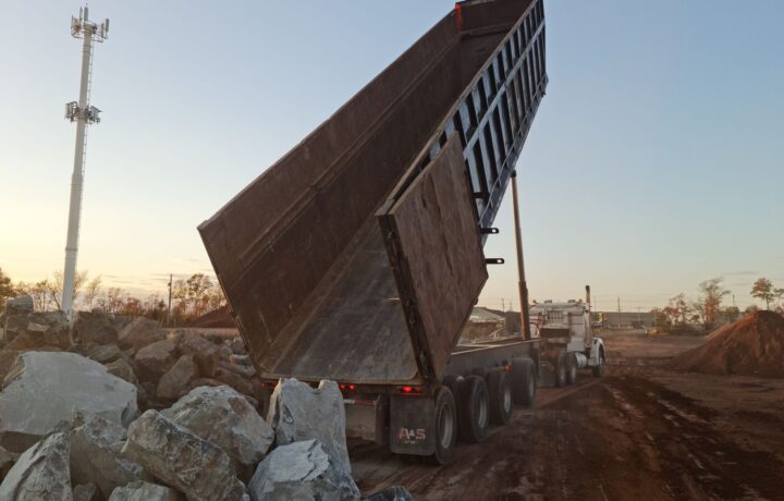 A dump truck unloading rocks at a construction site during sunset.