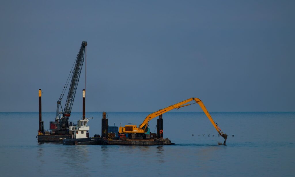 Dredging barge with crane operating at sea under clear sky.
