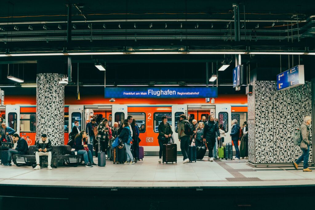Passengers wait on the platform at Frankfurt am Main Flughafen train station with a regional train in the background.
