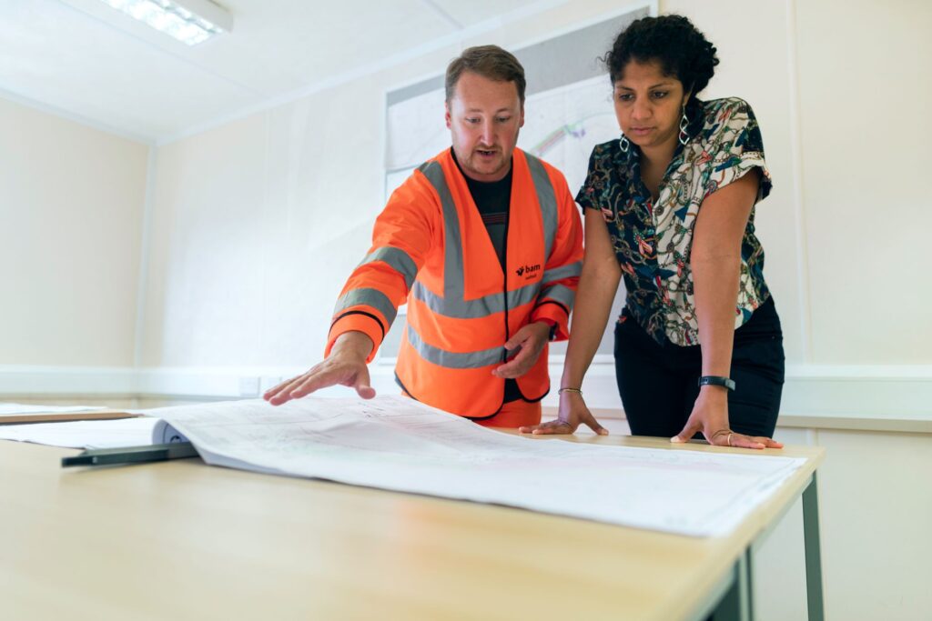 Two engineers reviewing blueprints in an office, discussing project details.