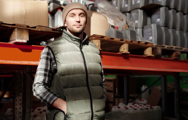 A man in a green vest stands confidently in a warehouse, illuminated by natural light.