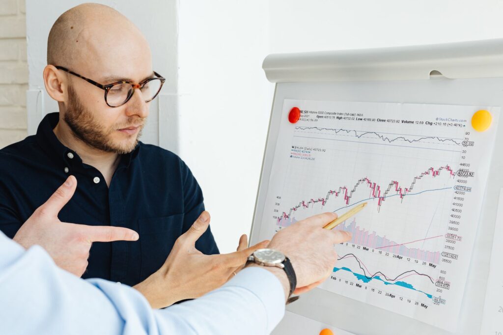 Business professionals discussing financial graphs on a flipchart during a daylight meeting.