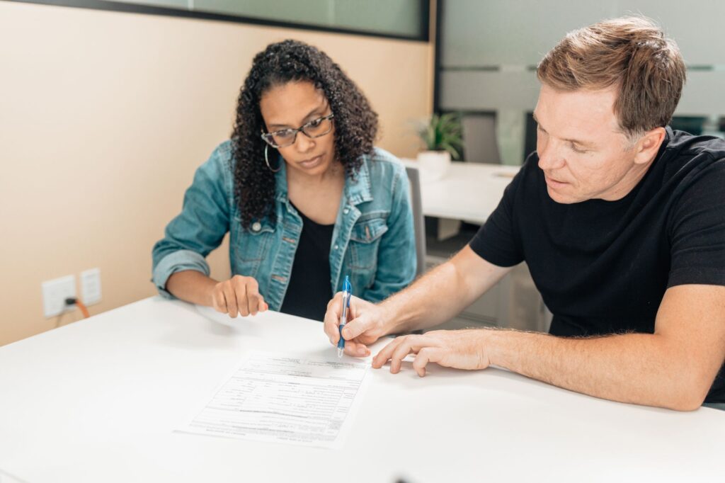 A couple working together to sign important legal documents at a desk in an office setting.