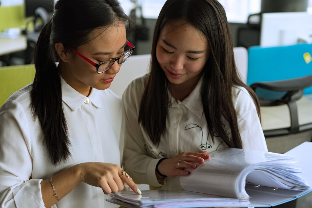 Two young women collaborating on a project in a modern office environment, emphasizing teamwork and productivity.