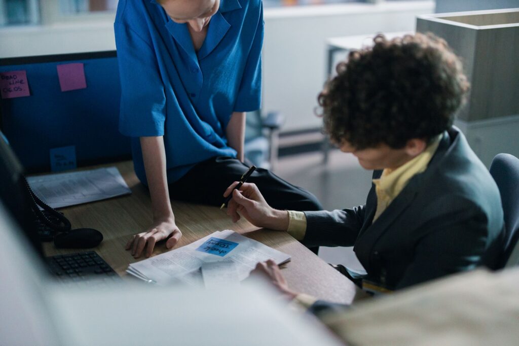 Two colleagues in a modern workspace discussing and writing notes during a meeting.