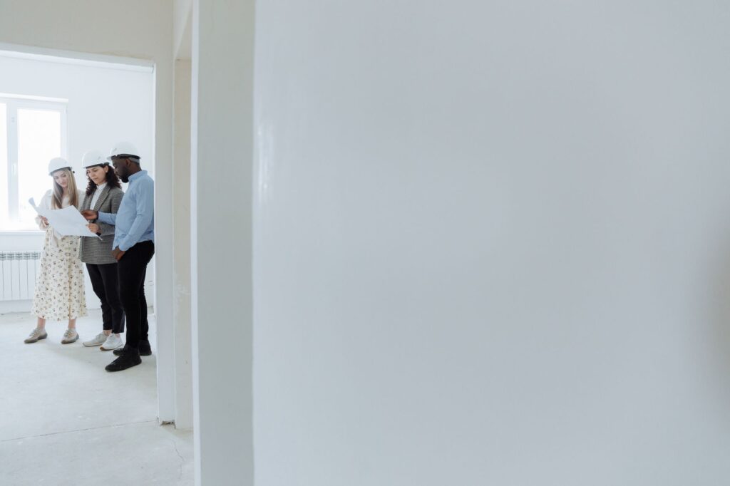 Architects wearing hard hats review blueprints inside a building under construction.